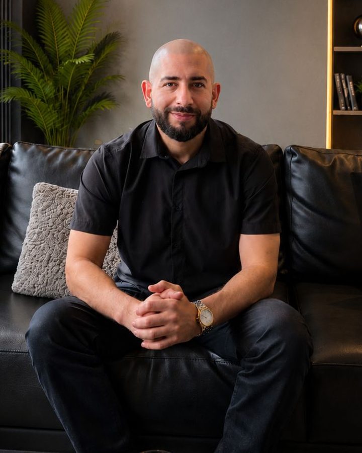 Michael Heredia at a workspace at golden hour, monitors glowing in violet and cyan